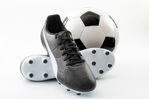 Competitive team sports, active life hobbies and athletic gear concept with old-fashioned black leather football cleats or athletics boots with laces and soccer ball isolated on white background